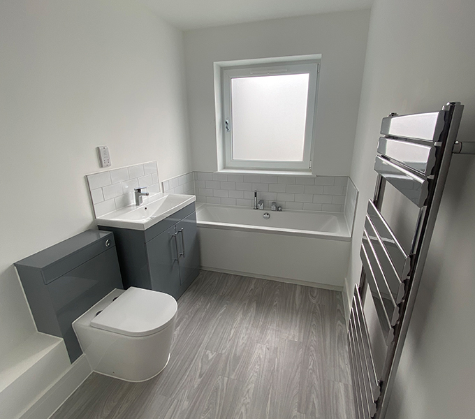 a white bathroom with a toilet, sink bath and metal radiator, with a square window on the wall