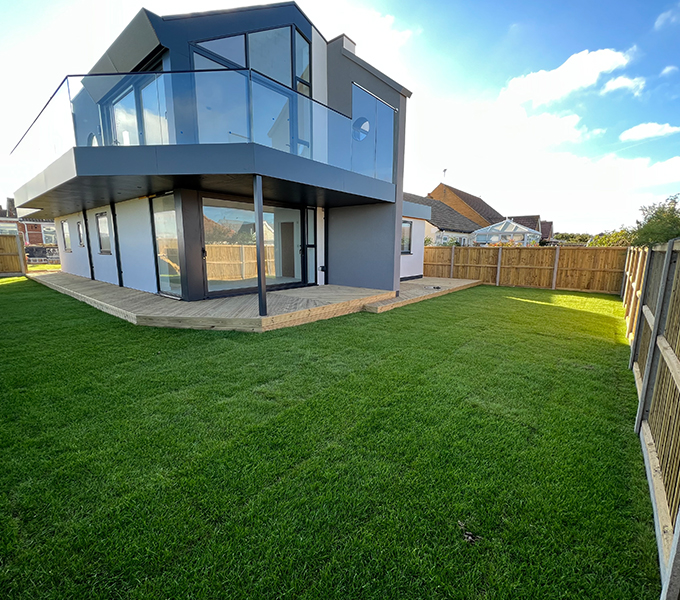 a modern house with an outdoor decking room with a lawn spreading around the corner