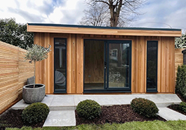 a garden room made of wood with glass doors and small bushes out front